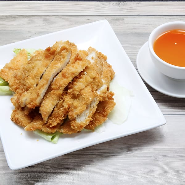 Crispy fried chicken cutlets on lettuce with a cup of hot tea on a wooden table.